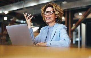 Witte vrouw staand achter laptop met telefoon in de hand